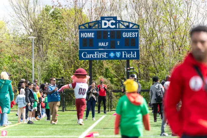 A field with kids, adults, and media people participating in Day of Play event